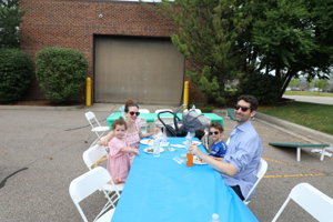 Family with two young children and a stroller seated at an outdoor table eating lunch
