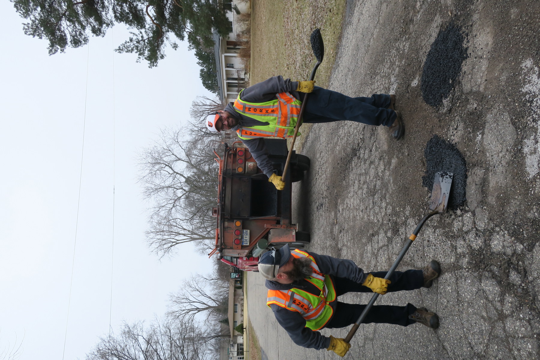 Two public works personnel filling potholes on a residential road
