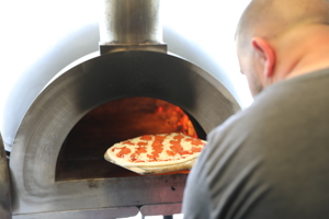 A man putting a pepperoni pizza into a pizza oven