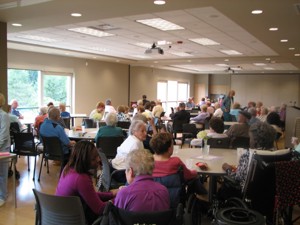 people gathered in a room of round tables enjoying conversation and beverages.