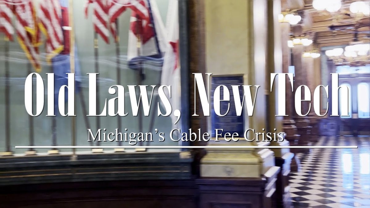 Video Title: Old Laws, New Tech: Michigan's Cable Fee Crisis over what looks to be a government capitol building with American flags in background.